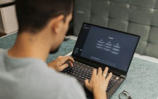 Inquadratura da dietro le spalle di un giovane uomo seduto a una scrivania mentre utilizza un computer portatile. Sullo schermo è chiaramente visibile l'interfaccia di ChatGPT.