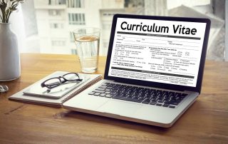 Postazione di lavoro minimalista: computer con curriculum, occhiali e agenda su un tavolo pulito.