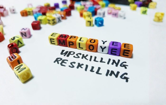 Primo piano di cubetti colorati che compongono la parola "EMPLOYEE" sopra le scritte a mano "UPSKILLING" e "RESKILLING" su un foglio bianco.