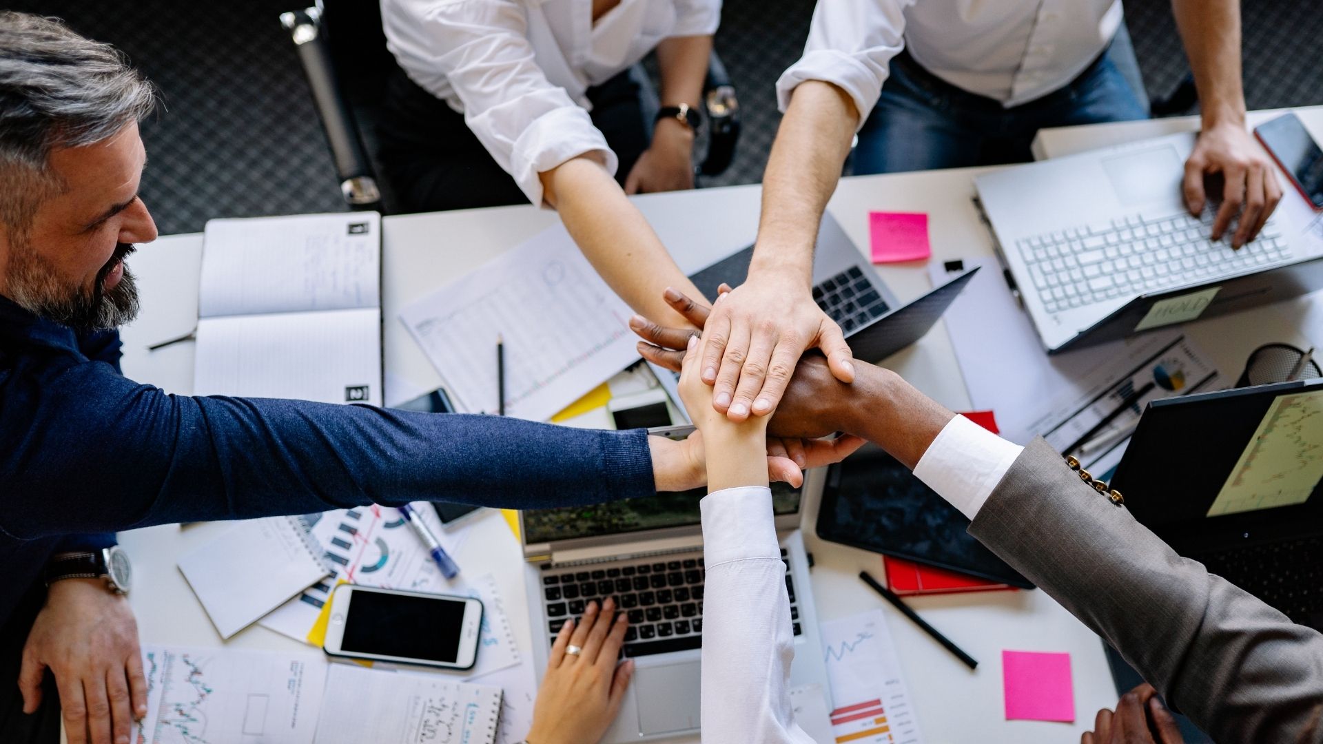 Un gruppo di professionisti che mette le mani insieme al centro di un tavolo da lavoro, a simboleggiare il successo del team e la cooperazione aziendale.