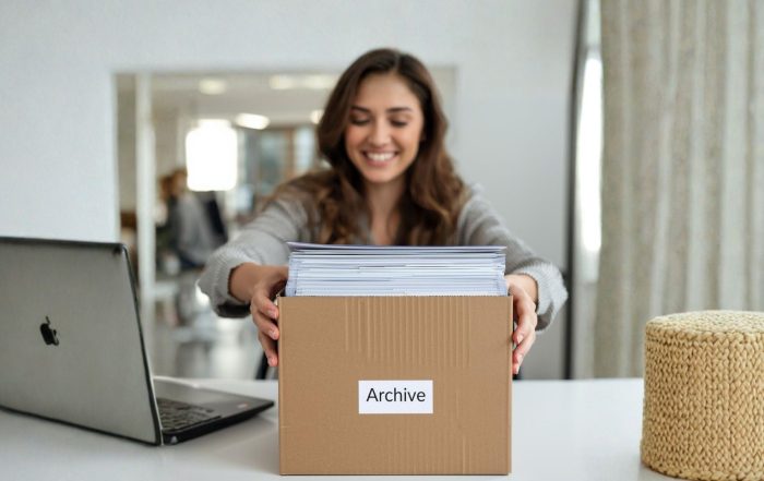 Una ragazza in un ufficio luminoso ripone vecchi documenti in uno scatolone con la scritta 'Archivio', mostrando un'espressione felice.