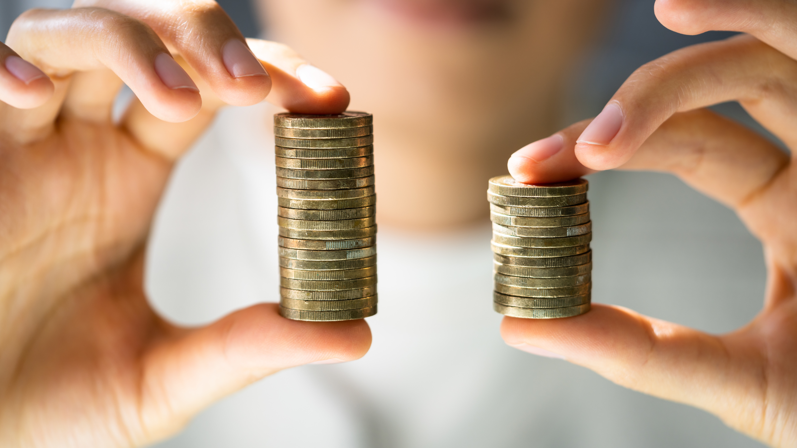 trasparenza-retributiva Close-up di due mani che tengono due pile di monete di altezza diversa, simbolo di disparità salariale e disuguaglianza economica.